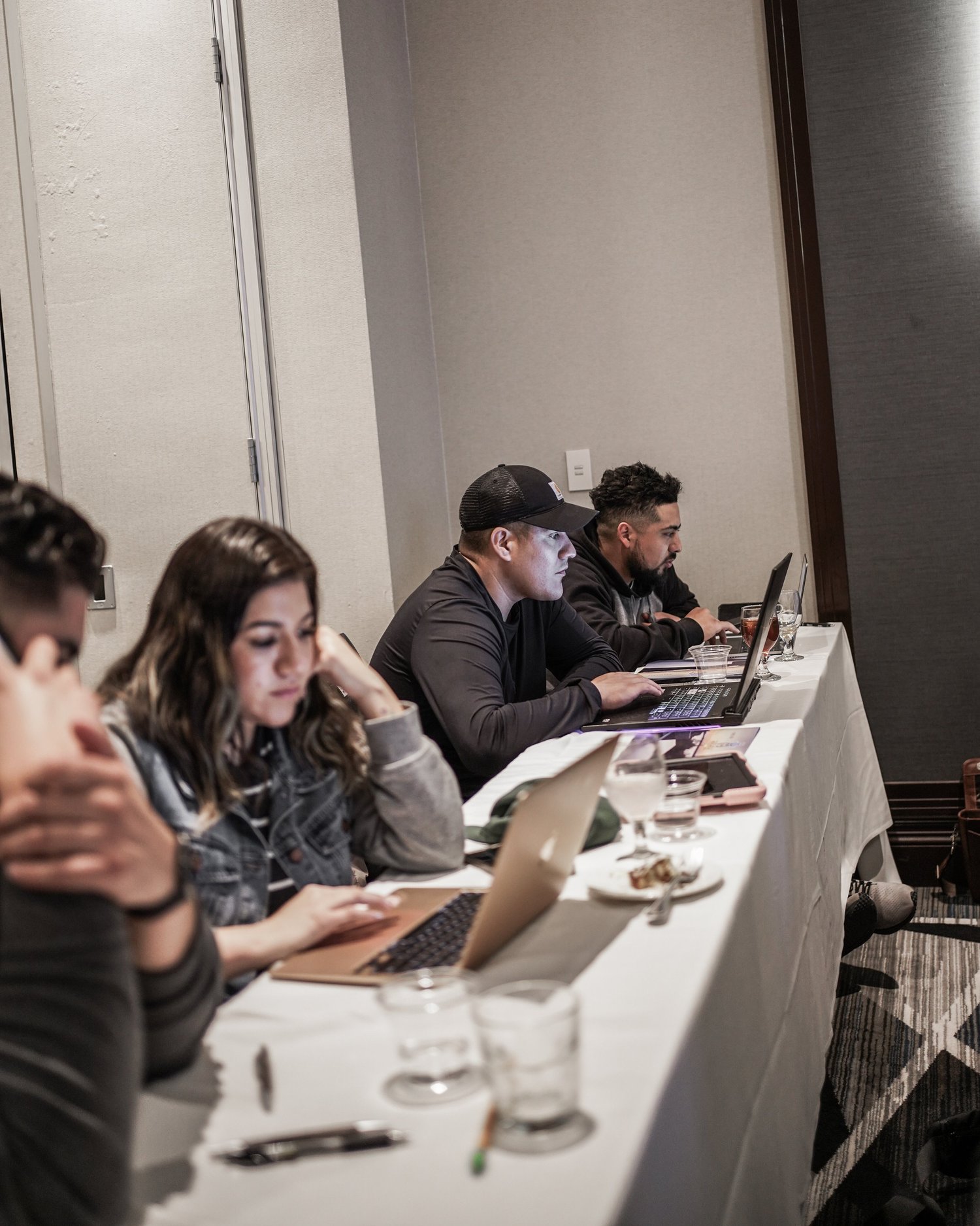 A group of people sitting at a long conference table working on laptops and tablets.