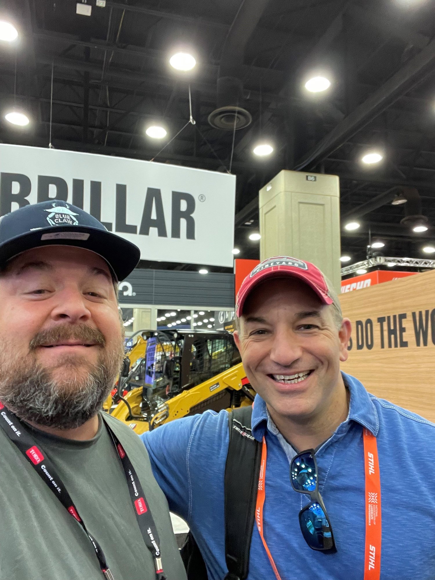 Ian McCarthy and Bob Maffei at the Equip trade show with equipment and signage in the background.