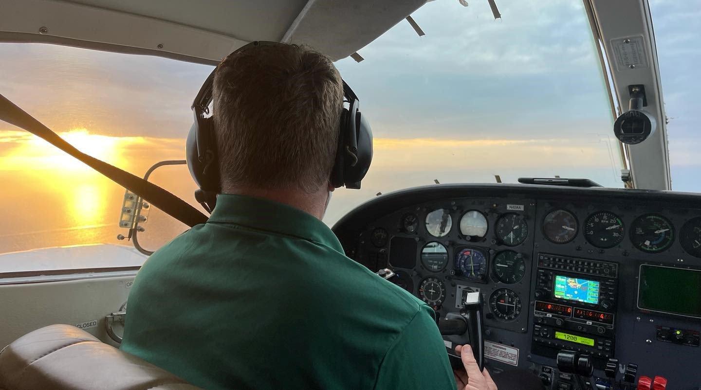 Pilots flying a small airplane during sunset, with dashboard instruments visible inside the cockpit.