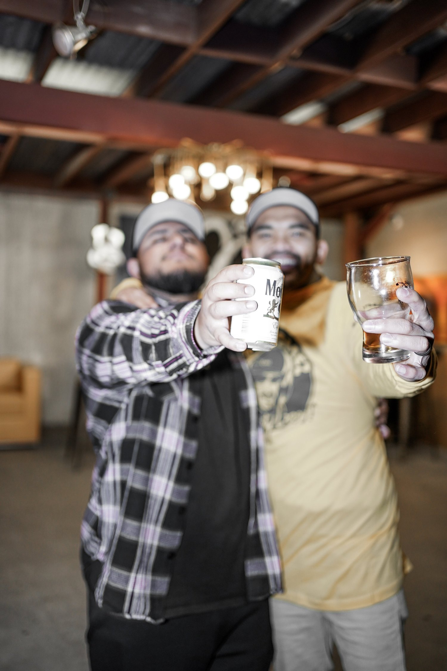 Two men celebrating with drinks in a rustic indoor space, smiling and toasting.